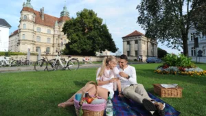 Ein Pärchen genießt ein romantisches Picknick auf einer Wiese vor dem historischen Schloss Güstrow an einem sonnigen Tag.