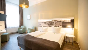 Helles Zimmer mit zwei grünen Sesseln und allergikerfreundlichem Designboden, ideal für entspannten und komfortablen Urlaub.