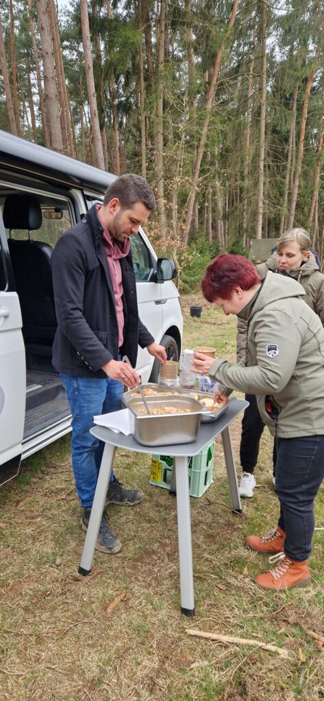 der Koch füllt Suppe in eine Schale vor dem Bulli im Wald zum Tag des Baumes